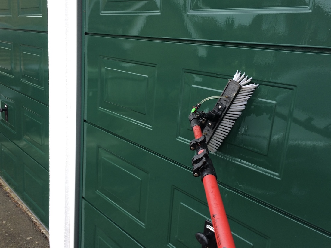 A green garage door being cleaned with a window cleaning brush.