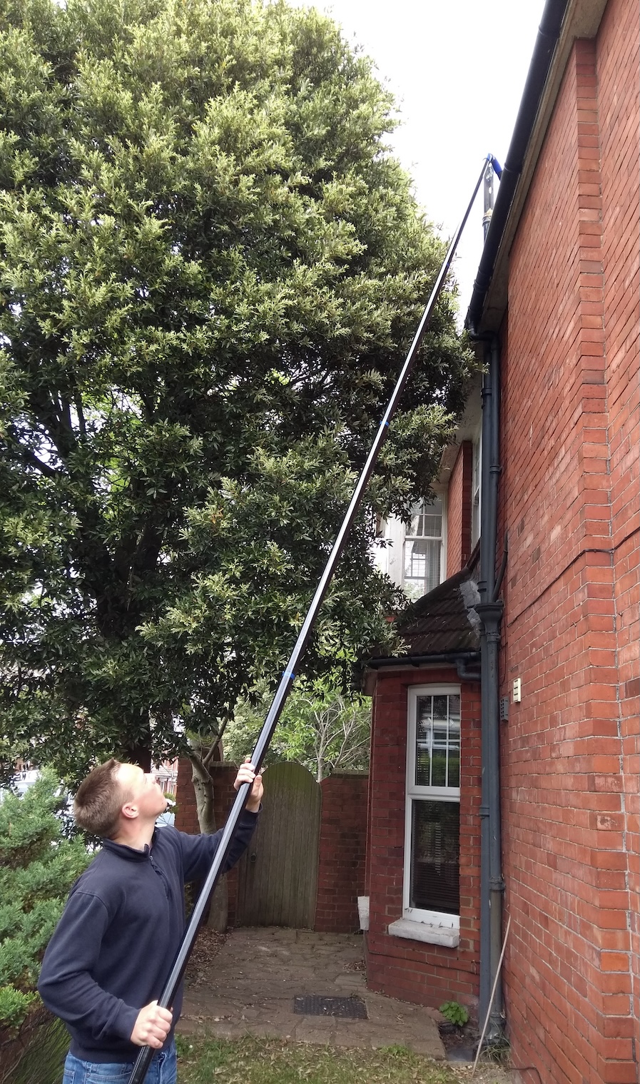 Cleaning gutters on a house from the ground using a long pole.