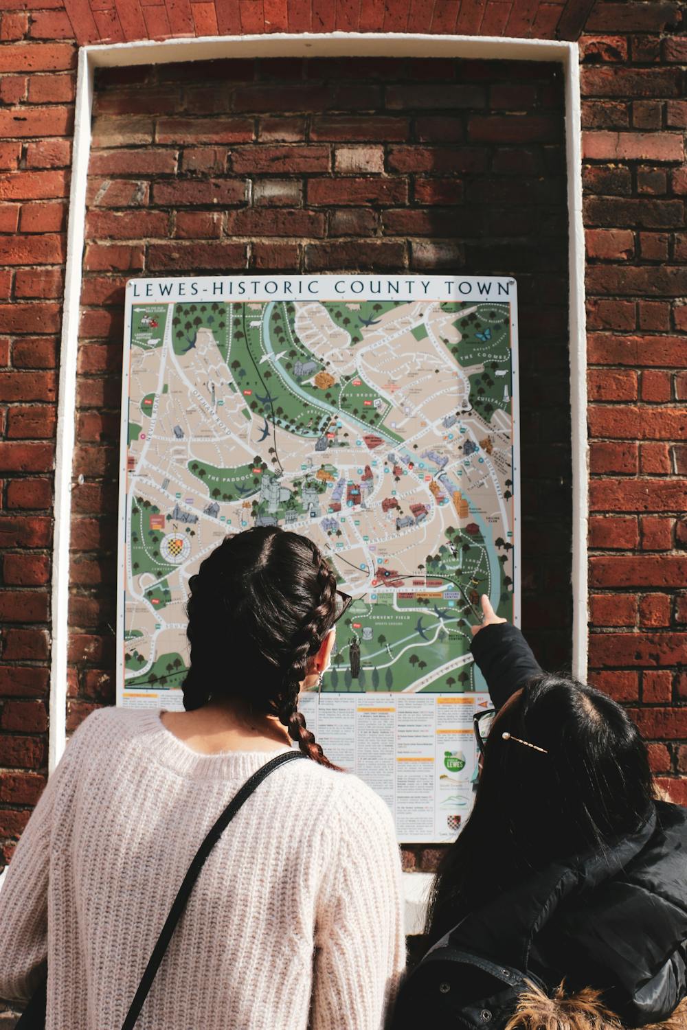 From behind, two women pointing to a map of Lewes on a wall.