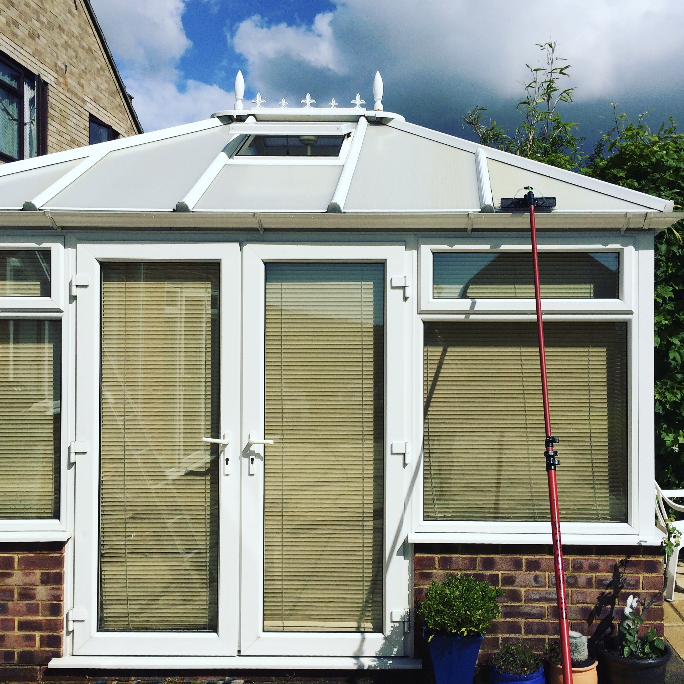 A cleaned conservatory from the outside with a water fed pole leaning up against it.