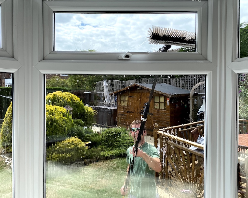 A man cleaning the front windows of a house with a pole.